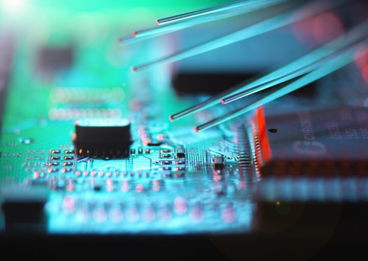Mehrere Glasfasern berühren eine elektronische Leiterplatte mit leuchtenden Schaltkreisen und Bauteilen.
