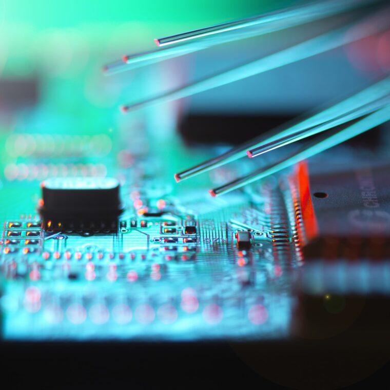 Mehrere Glasfasern berühren eine elektronische Leiterplatte mit leuchtenden Schaltkreisen und Bauteilen.