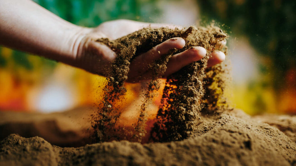 Hand lässt trockene Erde durch die Finger rieseln, bunter Hintergrund.