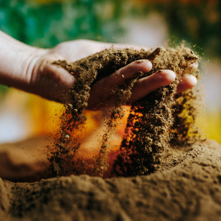 Hand lässt trockene Erde durch die Finger rieseln, bunter Hintergrund.