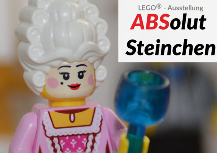 LEGO®-Figur einer adelig gekleideten Frau mit weißer Perücke und blauem Kelch. Rechts daneben Text: „LEGO®-Ausstellung ABSolut Steinchen“, wobei „ABS“ farblich hervorgehoben ist.