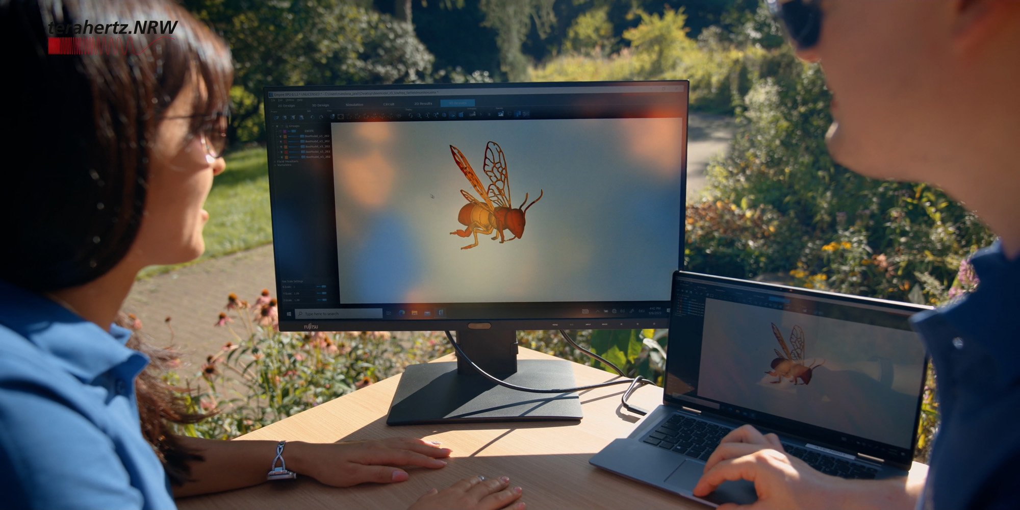 Zwei Personen arbeiten im Freien an einem Tisch mit Laptop und externem Monitor, auf dem eine 3D-Visualisierung einer Biene zu sehen ist; oben links ist das Logo von terahertz.NRW eingeblendet.