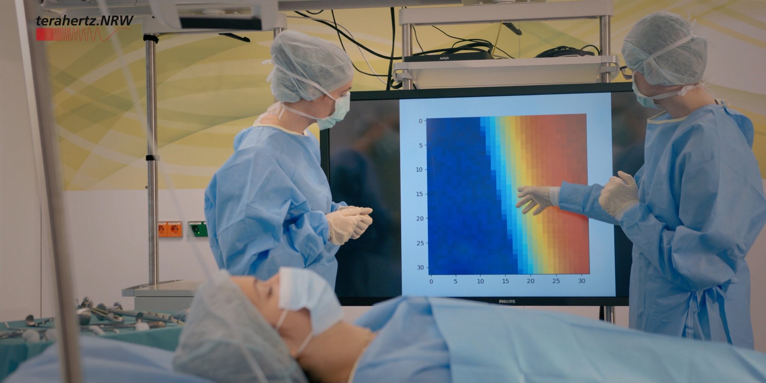 Zwei Chirurginnen vor Wärmebild-Grafik; im Vordergrund Patientin auf Operationstisch.