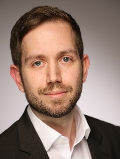 Dennis Pohle im Portrait. Er trägt ein weißes Hemd und dazu ein schwarzes Jackett.