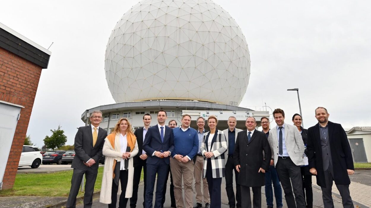 Gruppe von 14 Personen steht vor einer großen, kugelförmigen Radarkuppel mit geodätischer Struktur. Die Personen tragen überwiegend Businesskleidung und lächeln in die Kamera. Im Hintergrund ist ein Gebäude mit dem Logo des Fraunhofer-Instituts zu sehen.