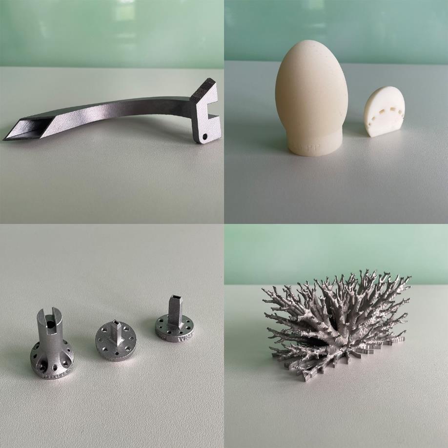 Vier Fotos von unterschiedlich geformten Bauteilen aus dem 3D-Druck, teils aus Metall, teils aus Kunststoff. Die Objekte zeigen komplexe Geometrien, darunter technische Komponenten und eine filigrane, korallenartige Struktur. Alle Objekte liegen auf einer hellen Oberfläche.
