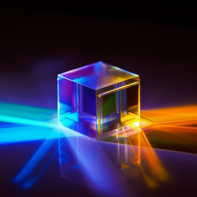 Lichtwürfel auf dunkler Fläche, der Lichtstrahlen in bunten Farben bricht und reflektiert.