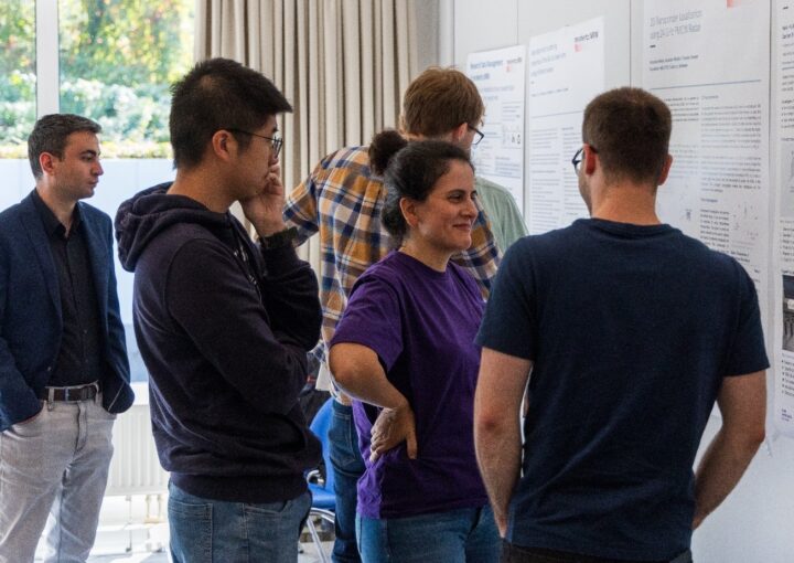 Mehrere Personen diskutieren vor wissenschaftlichen Postern. Im Vordergrund unterhält sich eine Frau im lila Shirt angeregt mit anderen Teilnehmenden.