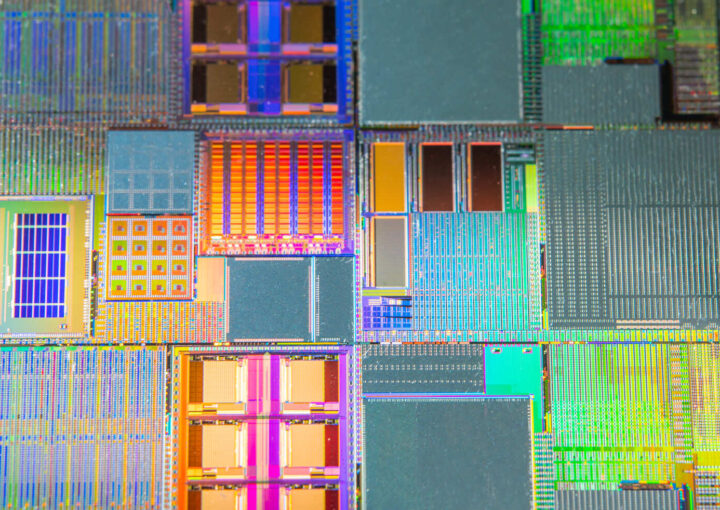 Makroaufnahme eines Mikrochips mit bunten, rechteckigen Strukturen und komplexen Schaltkreisen. Lichtreflexionen erzeugen farbige Muster.