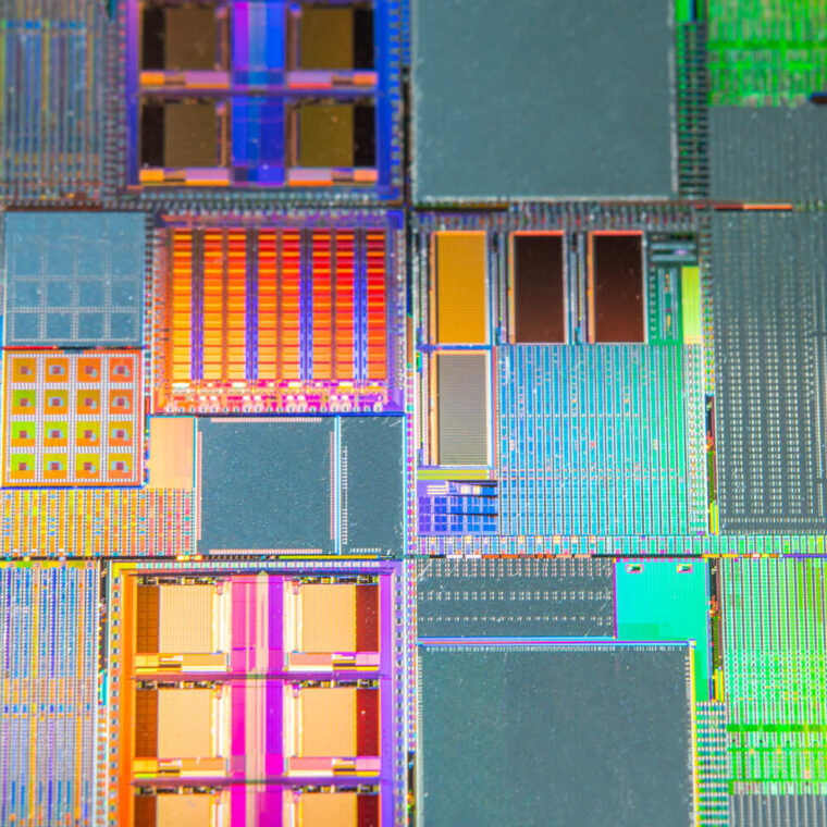 Makroaufnahme eines Mikrochips mit bunten, rechteckigen Strukturen und komplexen Schaltkreisen. Lichtreflexionen erzeugen farbige Muster.